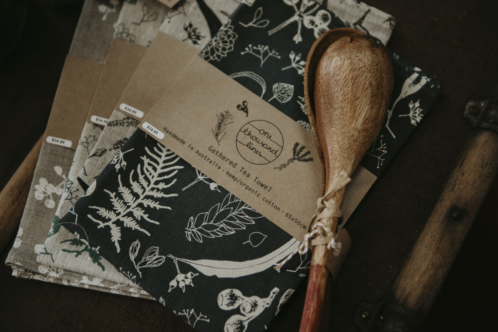 A pile of four handmade tea towels with wooden salad servers on top.