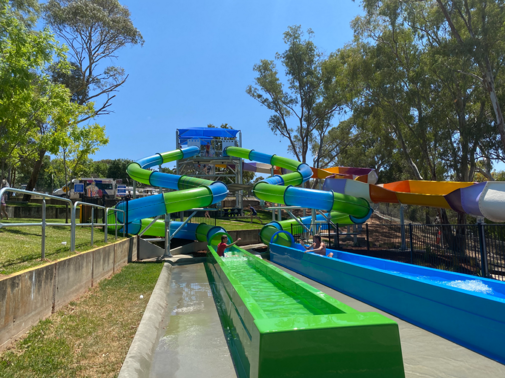 Image shows three colourful waterslides with swimmers emerging from two of them.