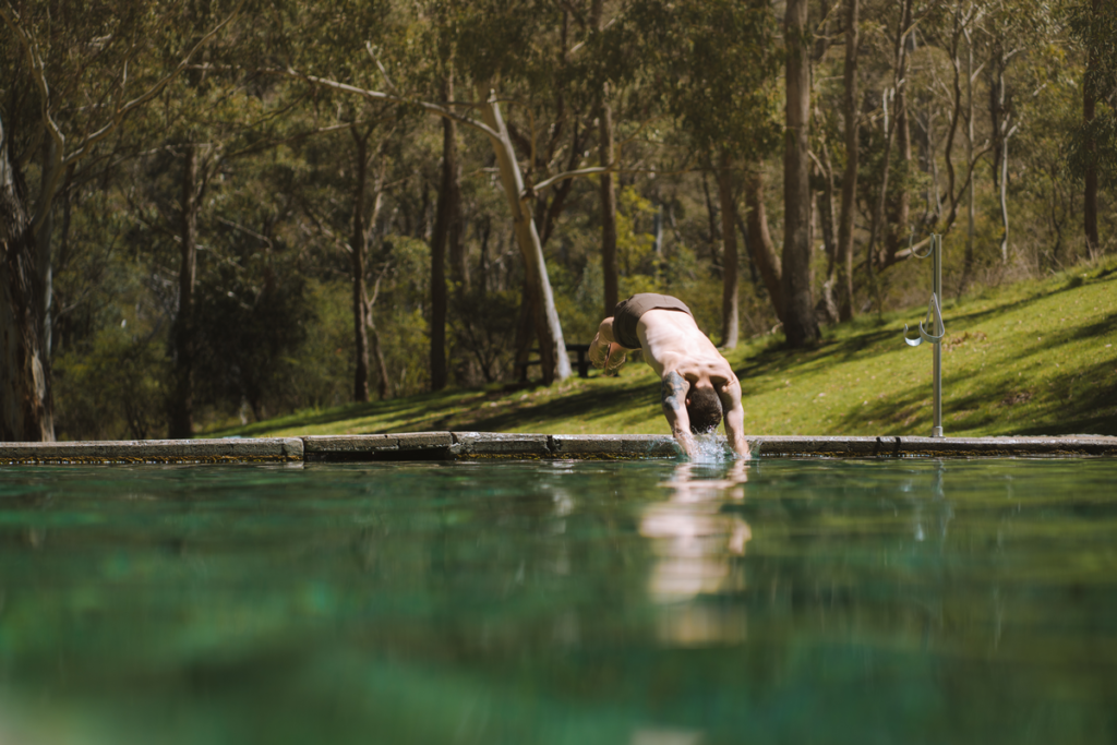 Image shows a man diving into a thermal pool, which is surrounded by forest.