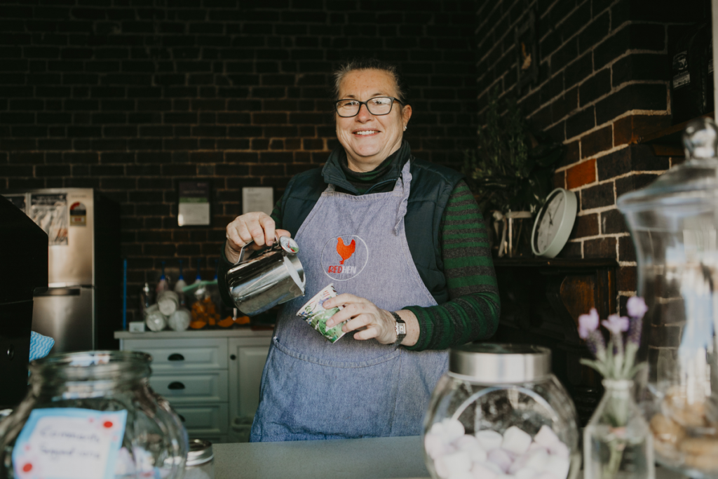 A friendly barista is pouring steamed milk from a milk frothing jug into a takeaway coffee cup.