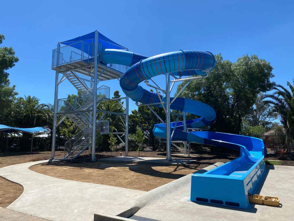 Image shows a large metal tower connected to a blue waterslide.